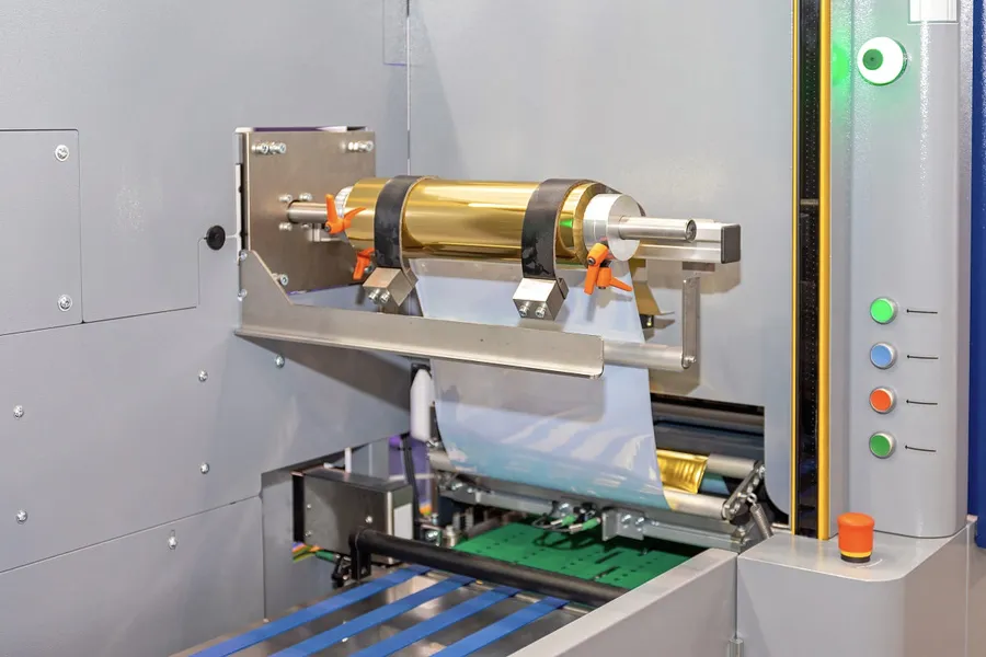 A reel of gold foil loaded on a foiling machine above a printed sheet