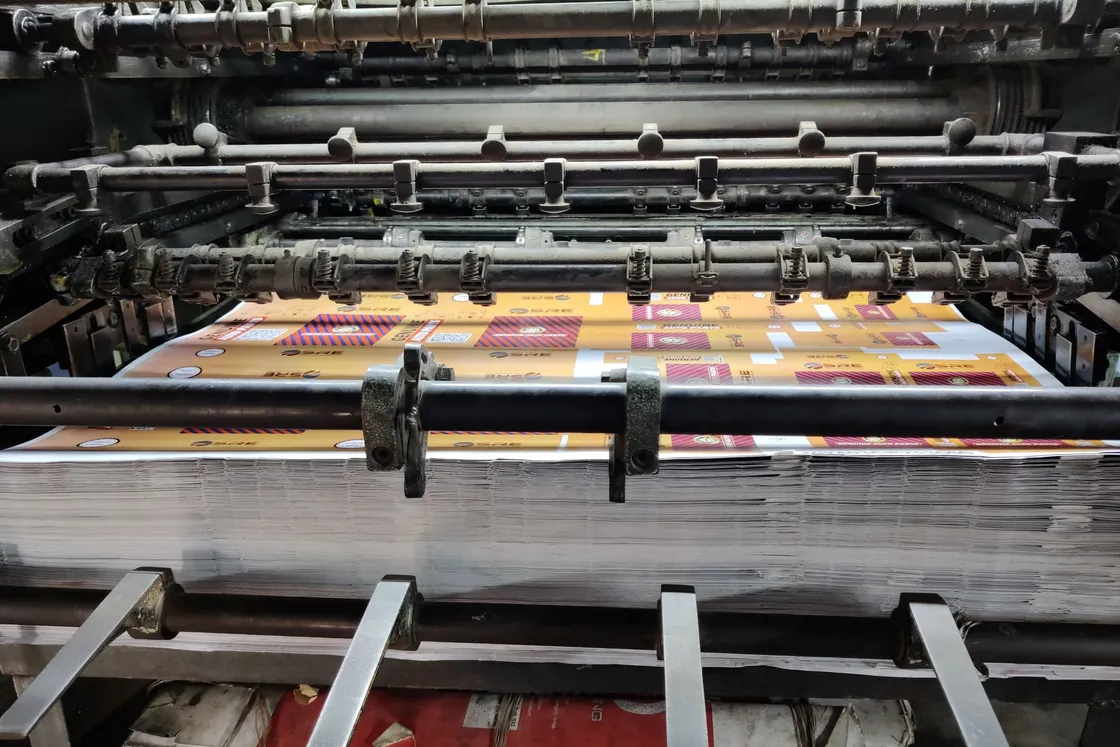 Printed label sheets coming off a press onto a stack of finished sheets