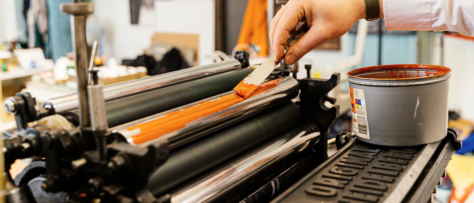 Orange ink being spread along the ink rollers of a printing press with a palette knife